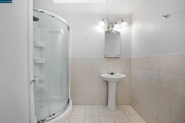 bathroom featuring an inviting chandelier, tile walls, a shower with shower door, and tile patterned flooring