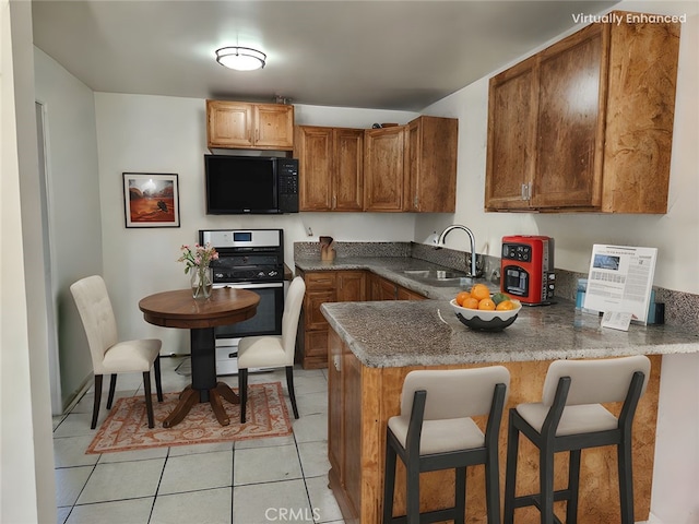 kitchen featuring black microwave, a kitchen bar, a peninsula, stainless steel gas range, and a sink