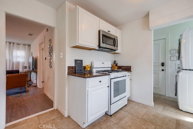 kitchen featuring white cabinets, stacked washer / dryer, light hardwood / wood-style floors, and white gas range