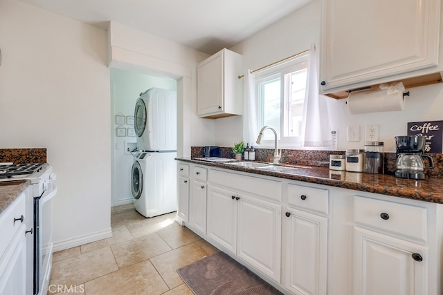 kitchen featuring dark stone counters, gas range gas stove, sink, white cabinetry, and stacked washing maching and dryer