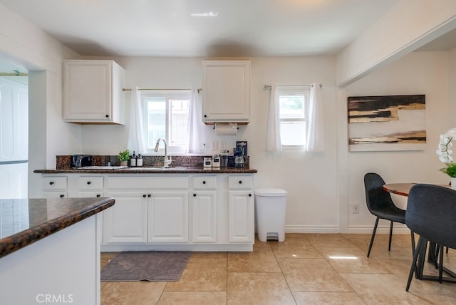 kitchen with dark stone countertops, a wealth of natural light, sink, and white cabinetry