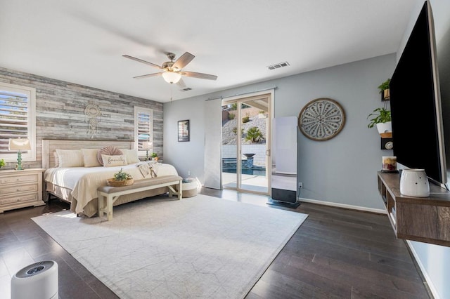 bedroom featuring access to outside, ceiling fan, dark wood-type flooring, and wooden walls