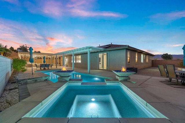 pool at dusk featuring an in ground hot tub, a patio area, and a fire pit