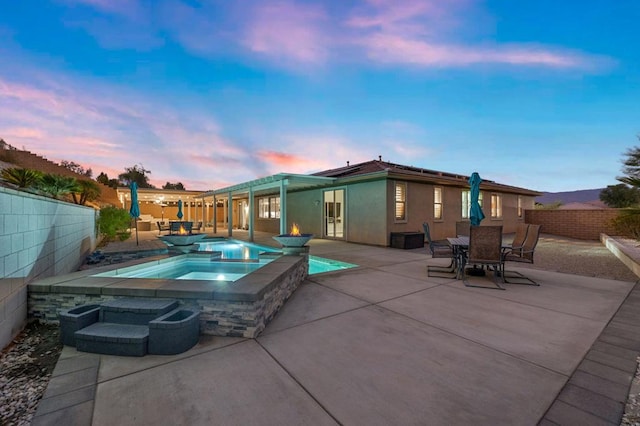 pool at dusk featuring an in ground hot tub and a patio