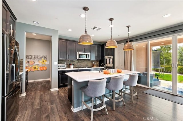 kitchen with dark brown cabinets, pendant lighting, a center island with sink, and stainless steel appliances