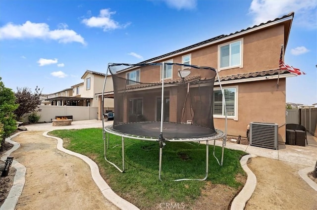 rear view of house featuring a lawn, central AC, a trampoline, and a patio area