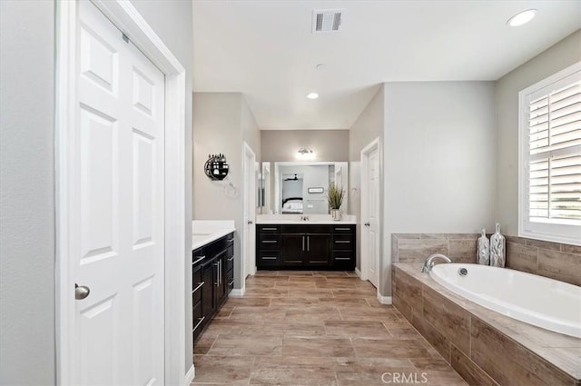 bathroom with a relaxing tiled tub, plenty of natural light, and vanity