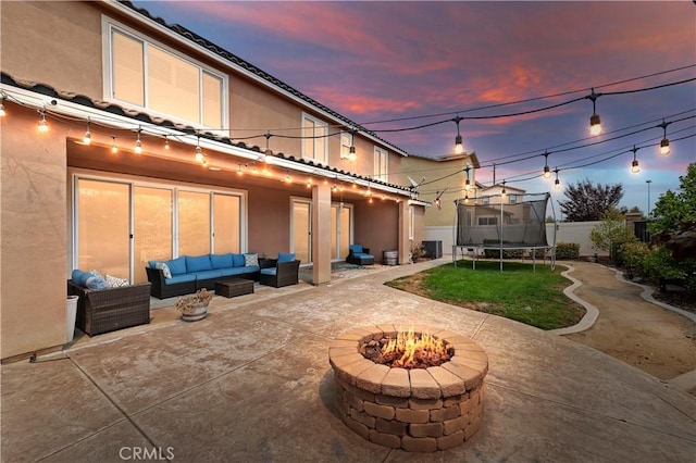 back house at dusk featuring a trampoline, a patio area, and an outdoor living space with a fire pit