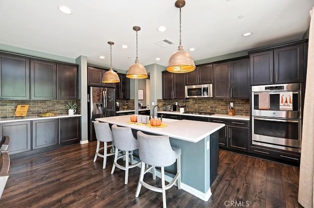 kitchen with pendant lighting, appliances with stainless steel finishes, dark hardwood / wood-style flooring, a center island with sink, and dark brown cabinets