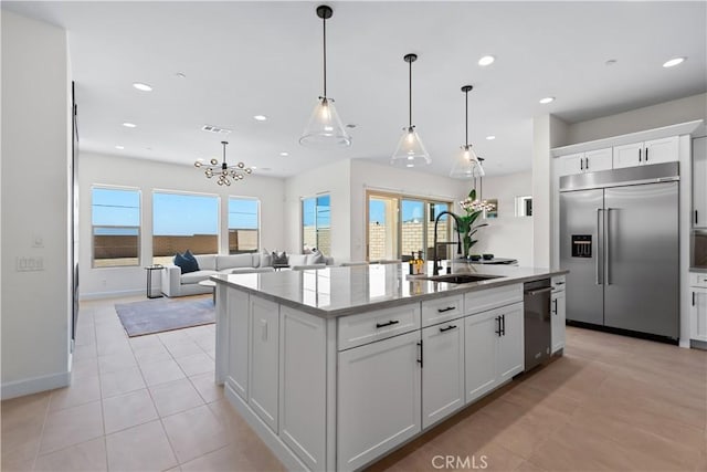 kitchen featuring stainless steel appliances, white cabinetry, hanging light fixtures, and a center island with sink