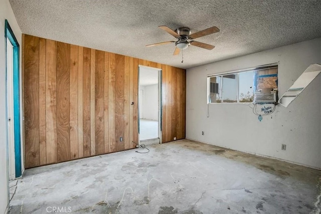 unfurnished bedroom with a textured ceiling, ceiling fan, cooling unit, and wood walls