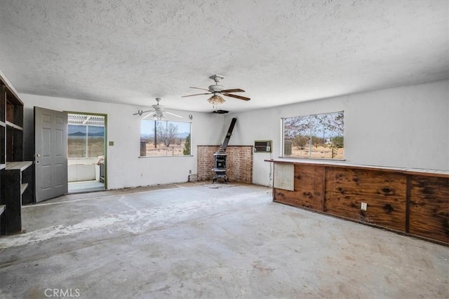 unfurnished living room featuring a healthy amount of sunlight, a wood stove, a textured ceiling, and an AC wall unit