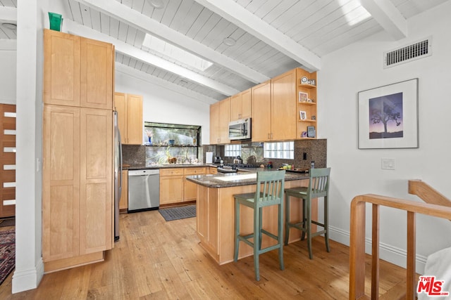 kitchen featuring vaulted ceiling with beams, appliances with stainless steel finishes, light wood-type flooring, and kitchen peninsula