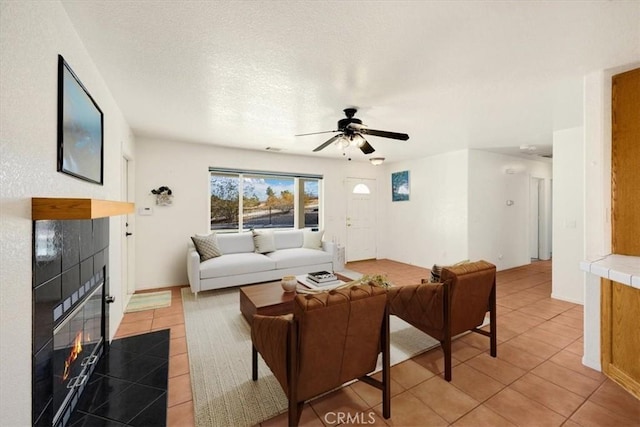 tiled living room with ceiling fan, a textured ceiling, and a fireplace