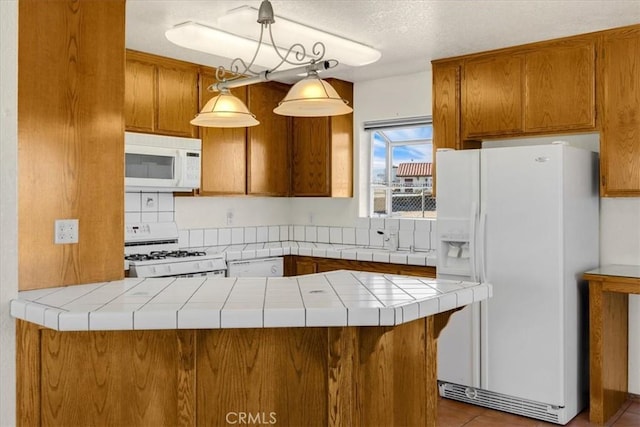 kitchen featuring hanging light fixtures, tile patterned flooring, tile counters, kitchen peninsula, and white appliances