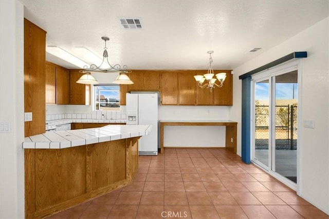 kitchen with decorative light fixtures, white refrigerator with ice dispenser, tile counters, kitchen peninsula, and an inviting chandelier