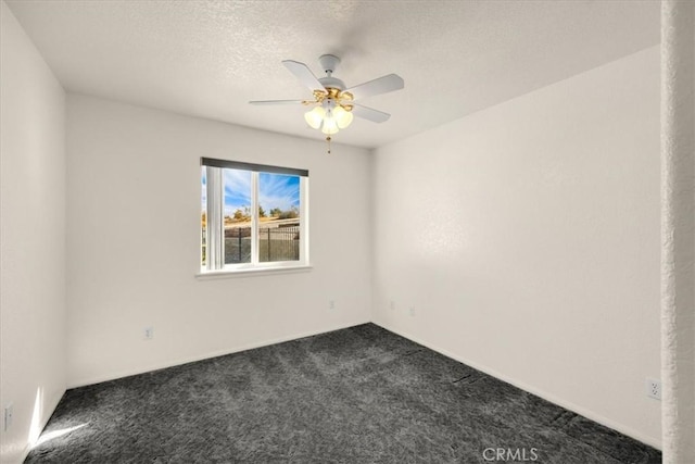 empty room featuring ceiling fan, dark carpet, and a textured ceiling