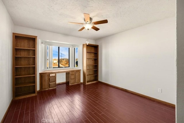 interior space with ceiling fan, dark hardwood / wood-style floors, built in desk, and a textured ceiling