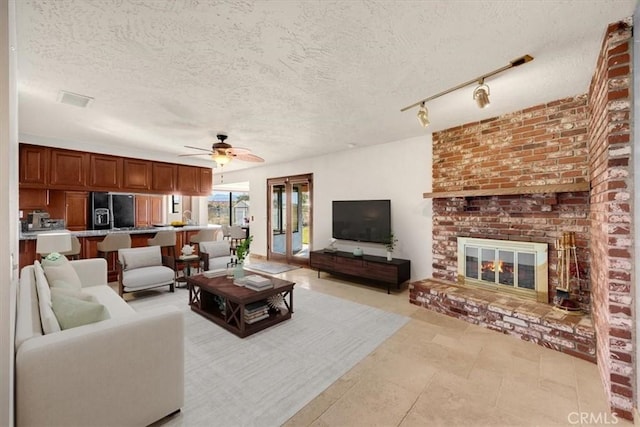 living room featuring ceiling fan, a brick fireplace, track lighting, and a textured ceiling