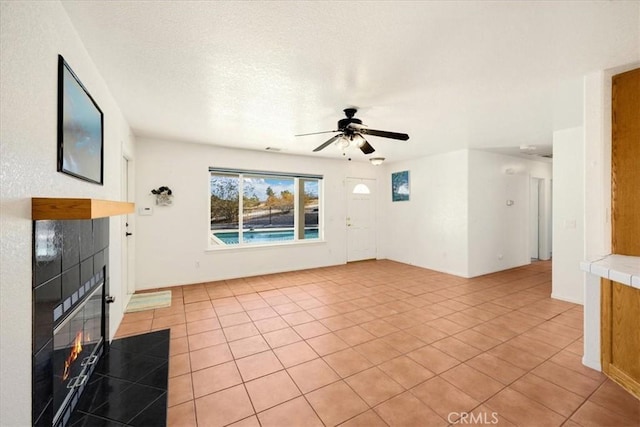 unfurnished living room with a tile fireplace, light tile patterned floors, a textured ceiling, and ceiling fan