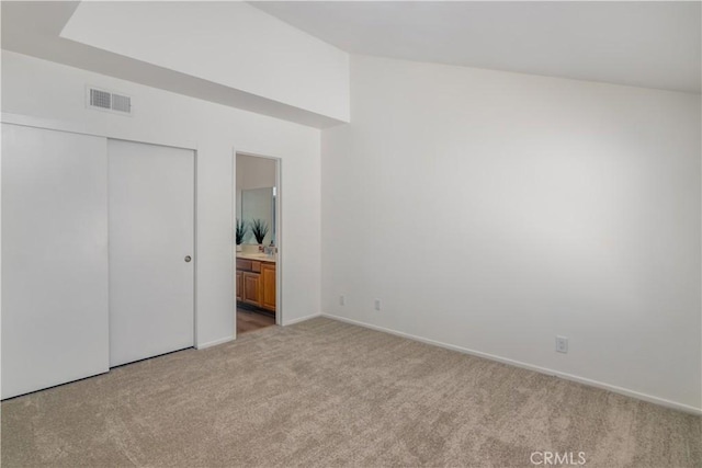 unfurnished bedroom featuring a closet, light colored carpet, and ensuite bath