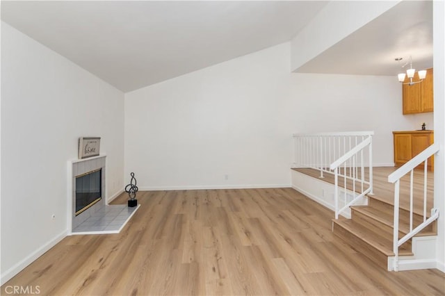 unfurnished living room featuring vaulted ceiling, an inviting chandelier, light hardwood / wood-style floors, and a fireplace