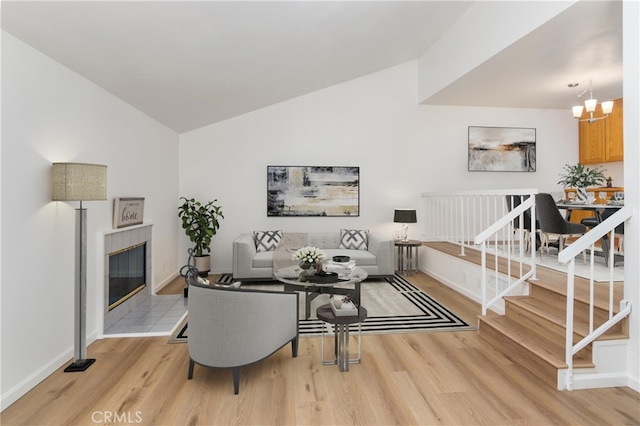 living room with lofted ceiling, light wood-type flooring, a notable chandelier, and a tile fireplace