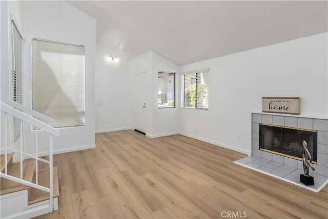 unfurnished living room featuring lofted ceiling, light hardwood / wood-style flooring, and a tile fireplace