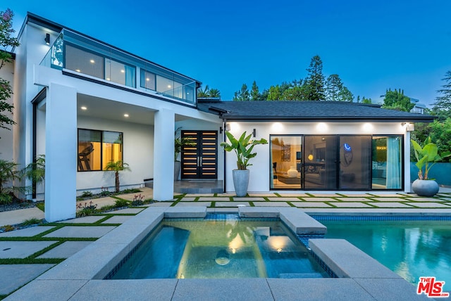 back house at dusk featuring a swimming pool with hot tub and a patio area