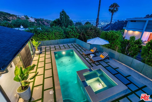 pool at dusk featuring an in ground hot tub and a patio area