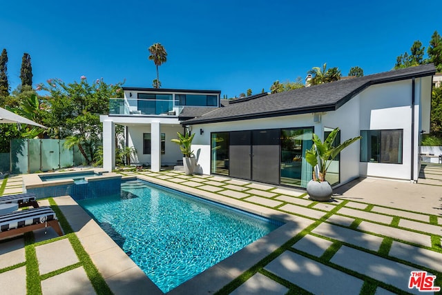 rear view of property with a pool with hot tub, a balcony, and a patio area