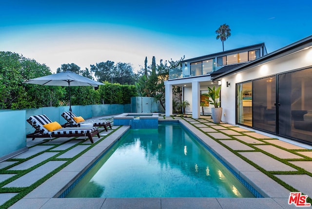 pool at dusk with an in ground hot tub and a patio area