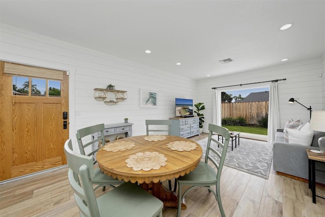 dining room with a wealth of natural light, wood walls, and light wood-type flooring