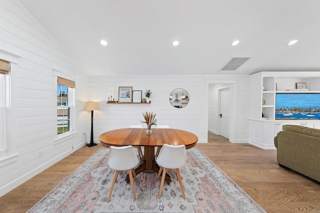 dining room featuring vaulted ceiling, light hardwood / wood-style flooring, and wooden walls