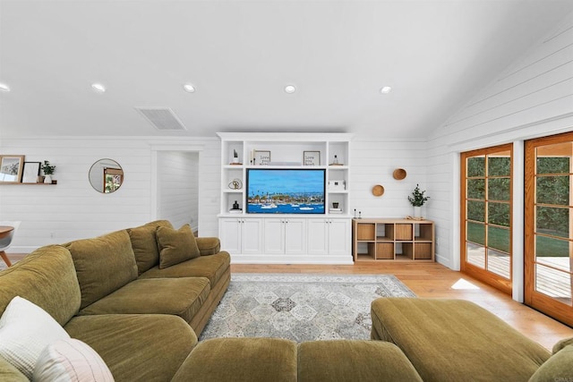 living room with light wood-type flooring, vaulted ceiling, and wooden walls