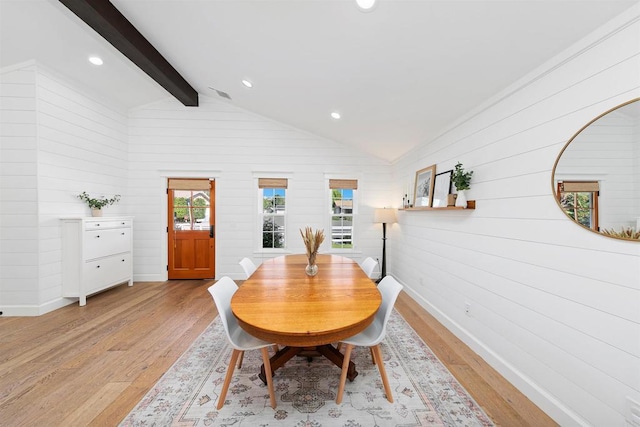 dining room featuring lofted ceiling with beams, wood walls, and light wood-type flooring