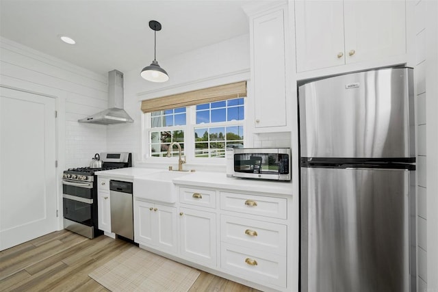 kitchen with white cabinets, light hardwood / wood-style flooring, wall chimney exhaust hood, decorative light fixtures, and stainless steel appliances