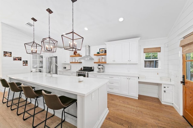 kitchen featuring white cabinets, appliances with stainless steel finishes, a large island with sink, and wall chimney range hood