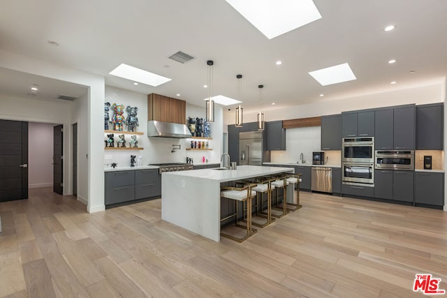 kitchen with appliances with stainless steel finishes, pendant lighting, ventilation hood, a kitchen bar, and a skylight