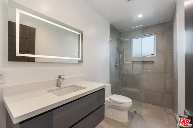 bathroom featuring a tile shower, vanity, and toilet