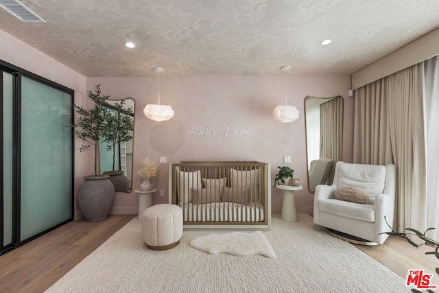 bedroom featuring a textured ceiling, a crib, and hardwood / wood-style flooring