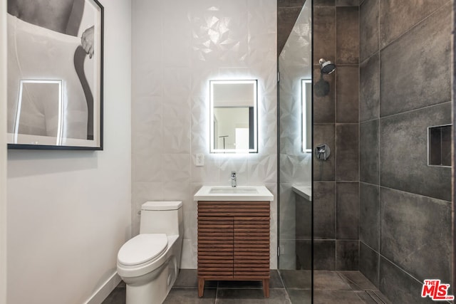 bathroom featuring vanity, toilet, a tile shower, tile walls, and tile patterned flooring