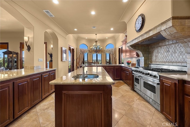 kitchen featuring backsplash, light stone countertops, double oven range, a kitchen island with sink, and sink