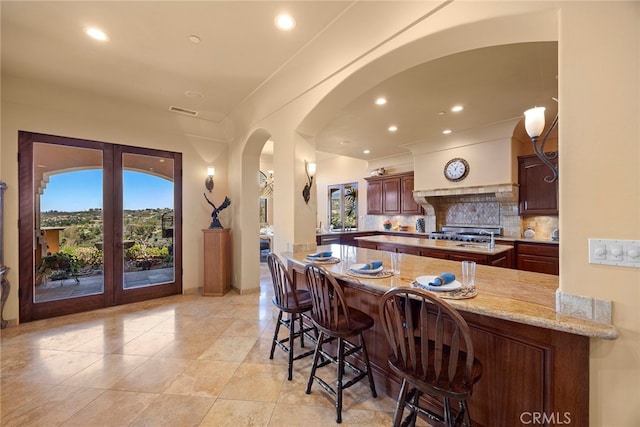 kitchen with light stone counters, kitchen peninsula, french doors, a kitchen bar, and decorative backsplash