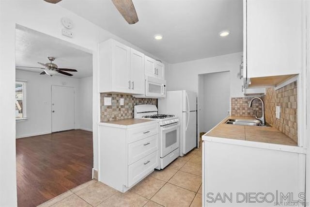 kitchen with white appliances, sink, light hardwood / wood-style flooring, decorative backsplash, and white cabinetry