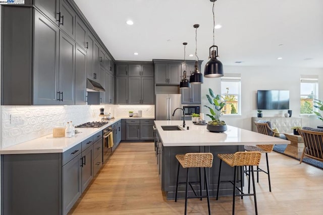 kitchen featuring pendant lighting, sink, light wood-type flooring, an island with sink, and stainless steel appliances