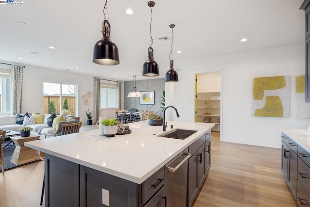 kitchen with dishwasher, a center island with sink, sink, hanging light fixtures, and light wood-type flooring