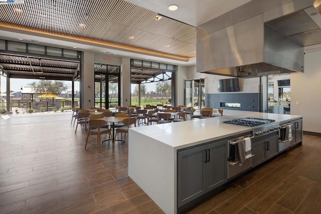 kitchen with gray cabinetry, a center island, stainless steel gas cooktop, dark hardwood / wood-style flooring, and island range hood