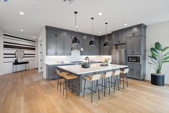 kitchen with pendant lighting, a breakfast bar, a spacious island, appliances with stainless steel finishes, and light hardwood / wood-style floors