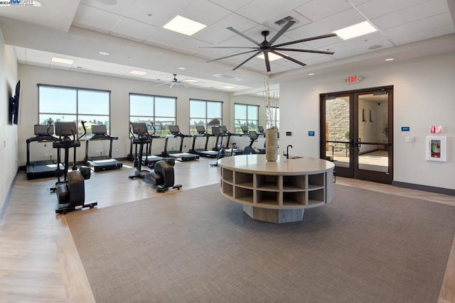 gym with a paneled ceiling, ceiling fan, and french doors